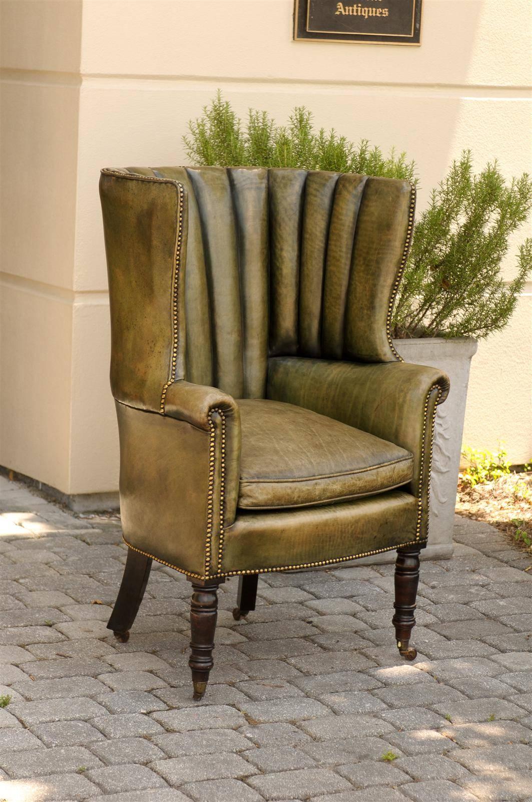 This English barrel wingback chair from the mid to late 19th century features an exquisite green toned leather upholstery with brass nails. The wing back offers privacy to the sitter, who can read a book quietly in front of a fireplace. The scrolled