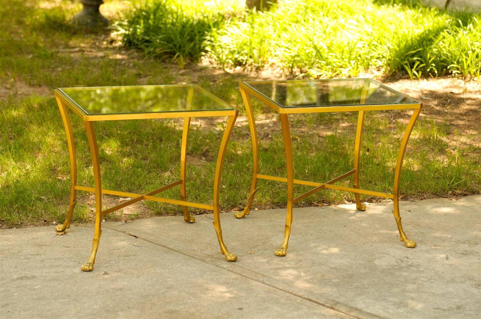 This pair of French Maison Baguès style drink tables features exquisite gilt bronze frames supporting square glass tops. Each table is raised on four saber type legs connected through a cross stretcher. The ensemble sits on delicate paw feet, the