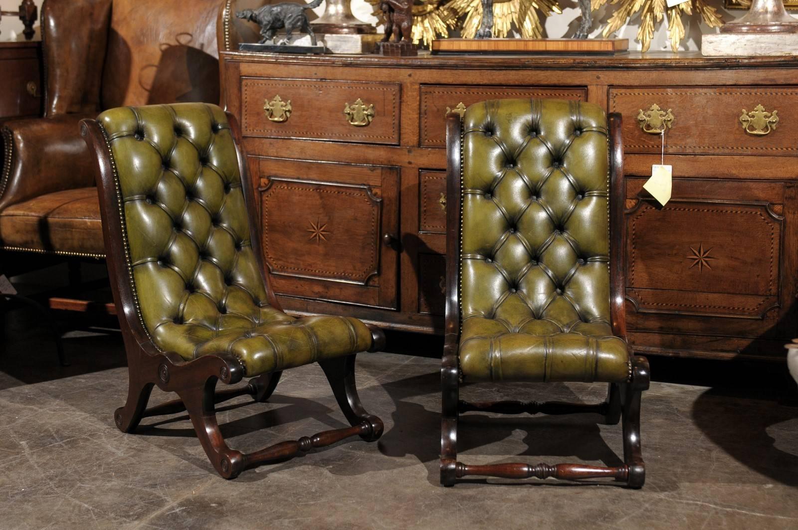 A pair of exquisite turn of the century English green tufted leather slipper chairs. This pair of English slipper chairs from the early 20th century features a green color tufted leather seat with nailhead riveting. The seats are nested into a curvy
