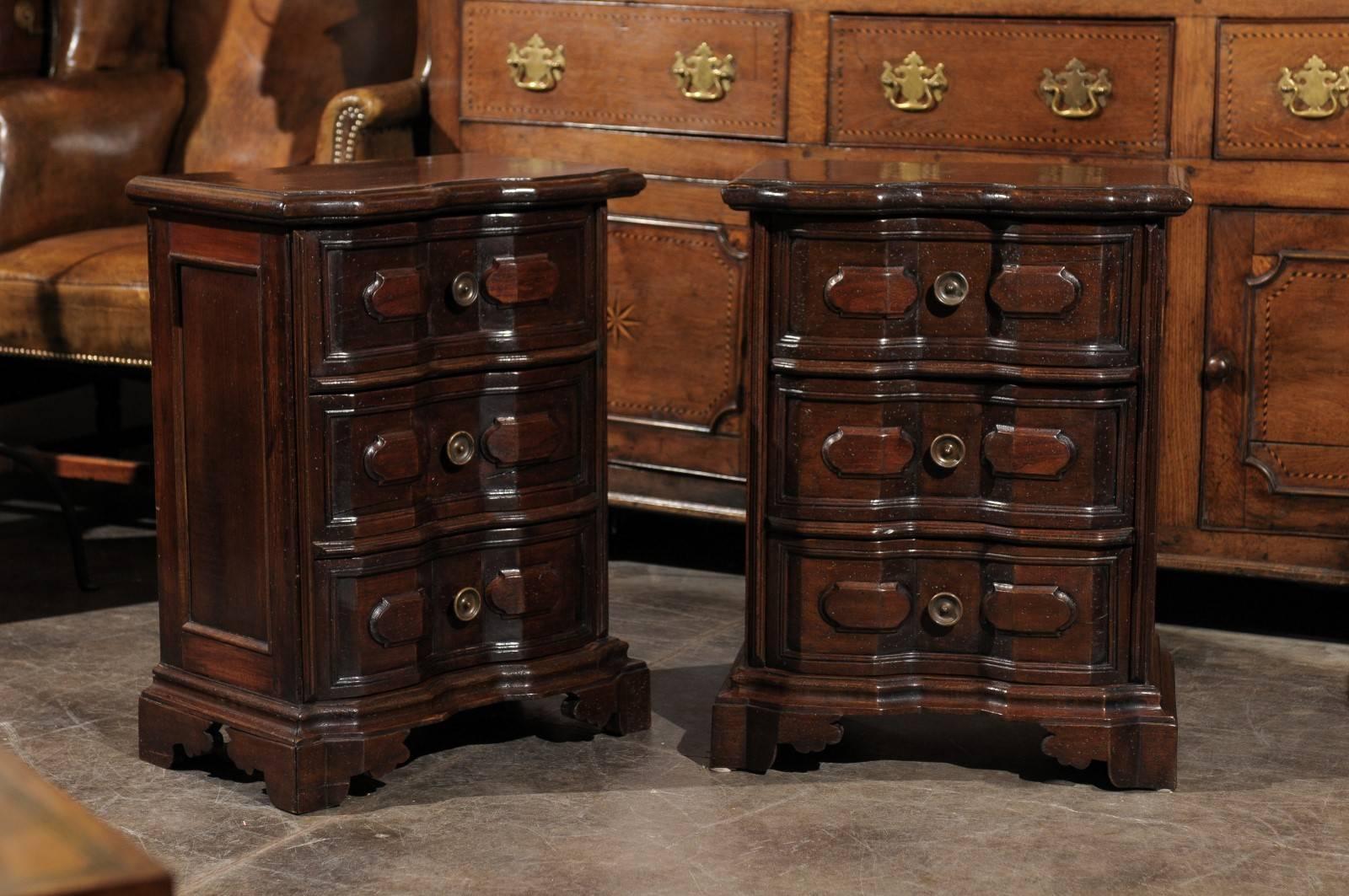 Each of this pair of Italian petite commodes features a two-plank rectangular molded top with a crossbow profile over a faceted conforming case fitted with three drawers complimented by two raised panels flanking a brass round knob. Molded panels