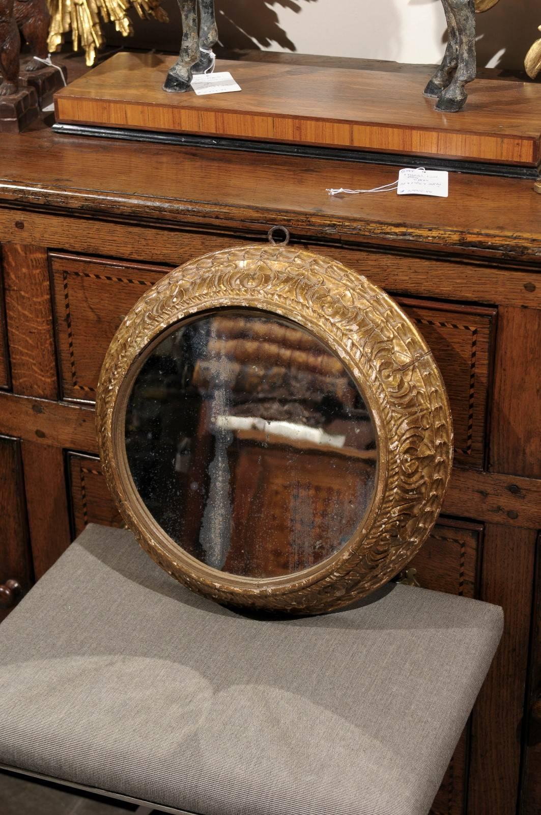 A pair of carved round English giltwood mirrors from the mid 19th century.  This pair of English midcentury round mirrors each features a flat round distressed mirror plate set within a two part giltwood molded frame with floral and beaded carving.
