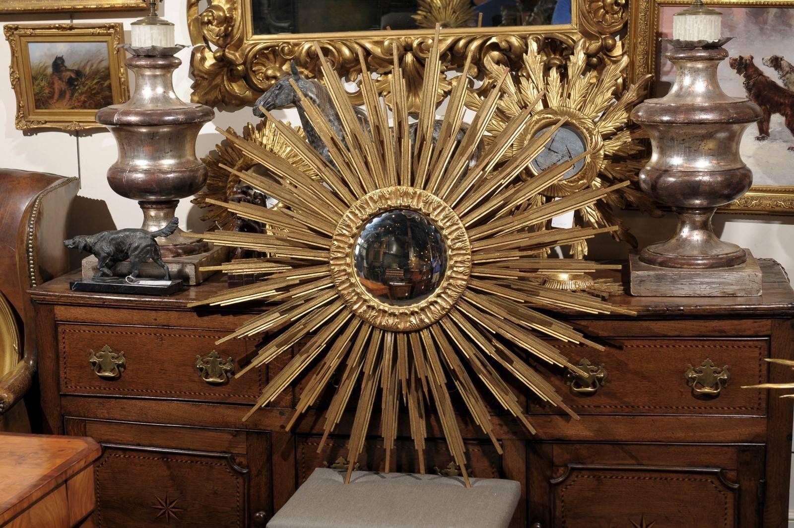 A French sunburst mirror with a convex round mirror plate framed by a gilt wood molded frieze of acanthus leaves from which figured beams radiate. The two layers of pointed and gradually thinner wooden rays evoke images of ostentatious religious