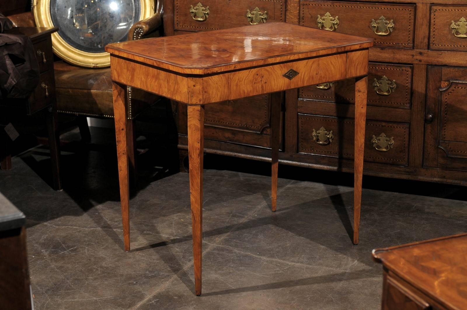 This 19th century Austrian Biedermeier wood table features a rectangular planked top with cross-banded inlay of darker wood surrounding the rim and canted corners. A diamond-shaped brass keyhole escutcheon compliments the center of the dovetailed