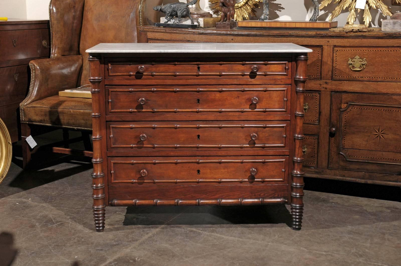 This 19th century English chest of drawers is adorned with a faux bamboo trim on both front and sides as well as the posts ending on unusual bobbin-turned feet at the front. The rectangular white marble top, presenting an incised line originally to