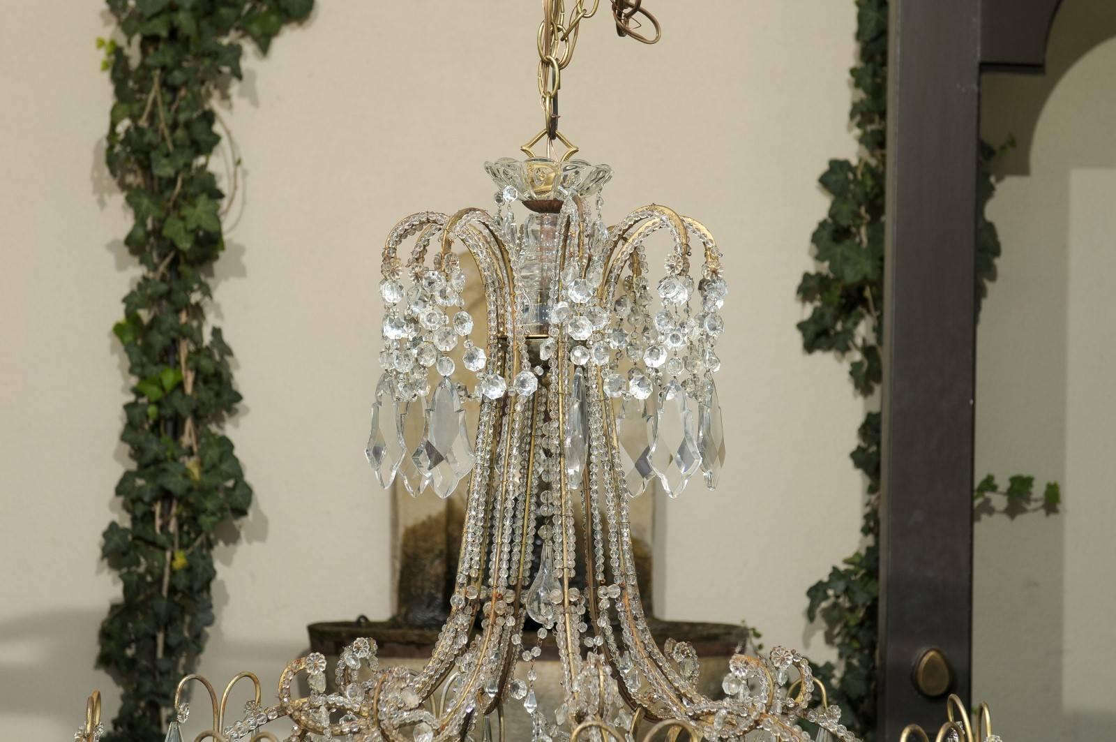 This large Italian gilt metal and crystal eight-light chandelier from the early 20th century features a cup-shaped central shaft with a hanging crystal sphere from which emerge crystal-beaded C-scrolled arms arranged on two levels. The upper arms,