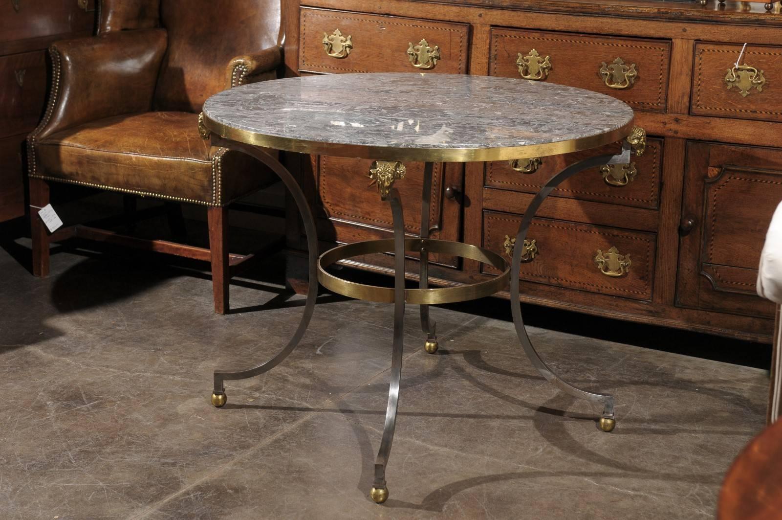 This French Directoire style round steel and brass end table from the mid 20th century features a stunning circular grey veined marble top surrounded by a brass frame. Four half moon steel legs are connected to the top with skillfully represented