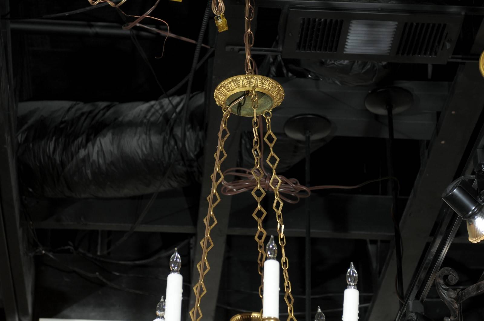 A small French Empire style metal chandelier from the beginning of the 20th century hung by three chains of diamond shaped links. Six ormolu arms shaped as eagle protomes emanate from the black finish central shaft culminating with an