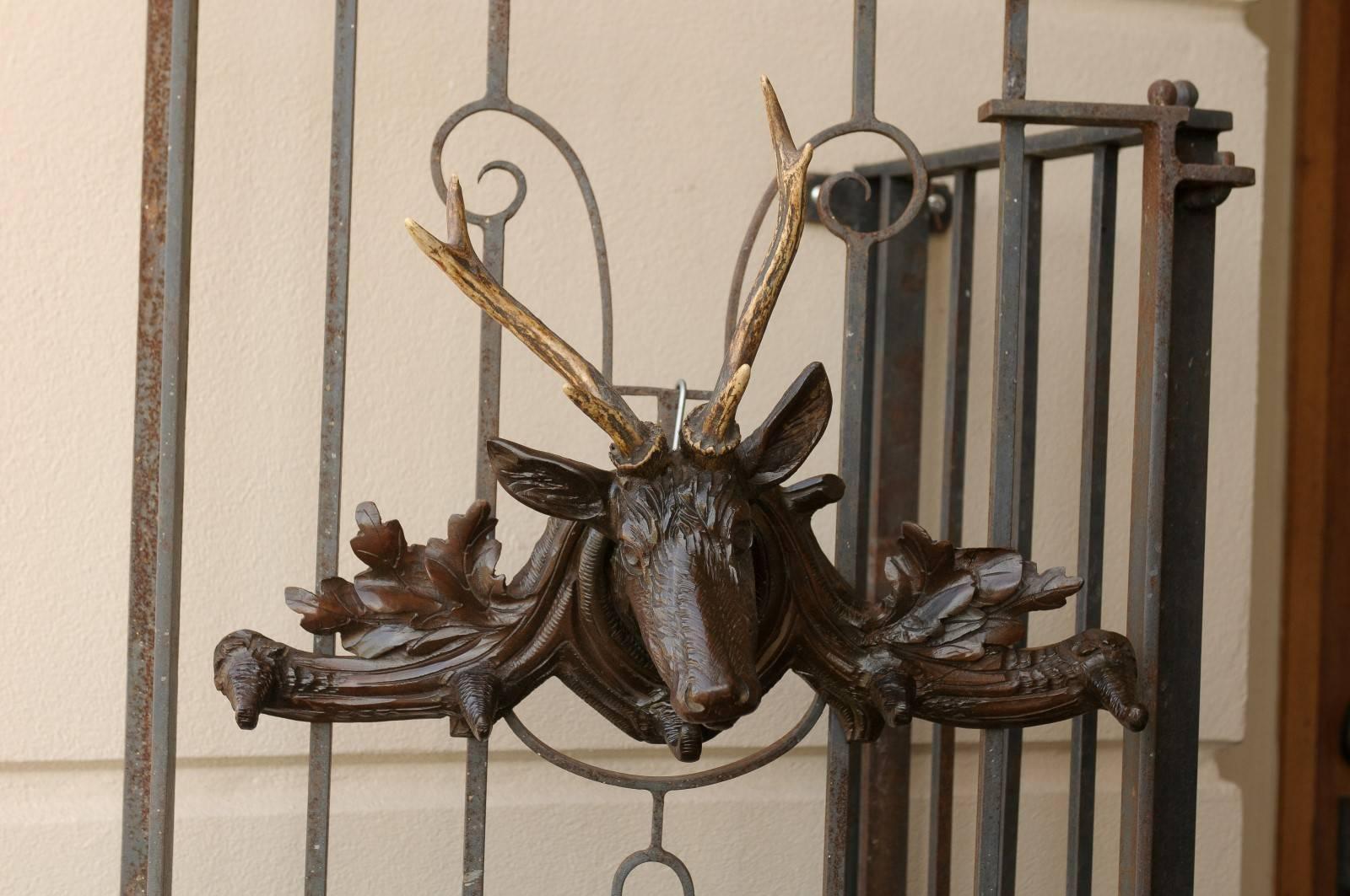 French turn of the century wall-mounted coat rack (also known as a hat rack) with carved deer and real antlers. This carved wood French hat rack circa 1900 features a deer head with real antlers. The arms of this dark wood coat rack are adorned with