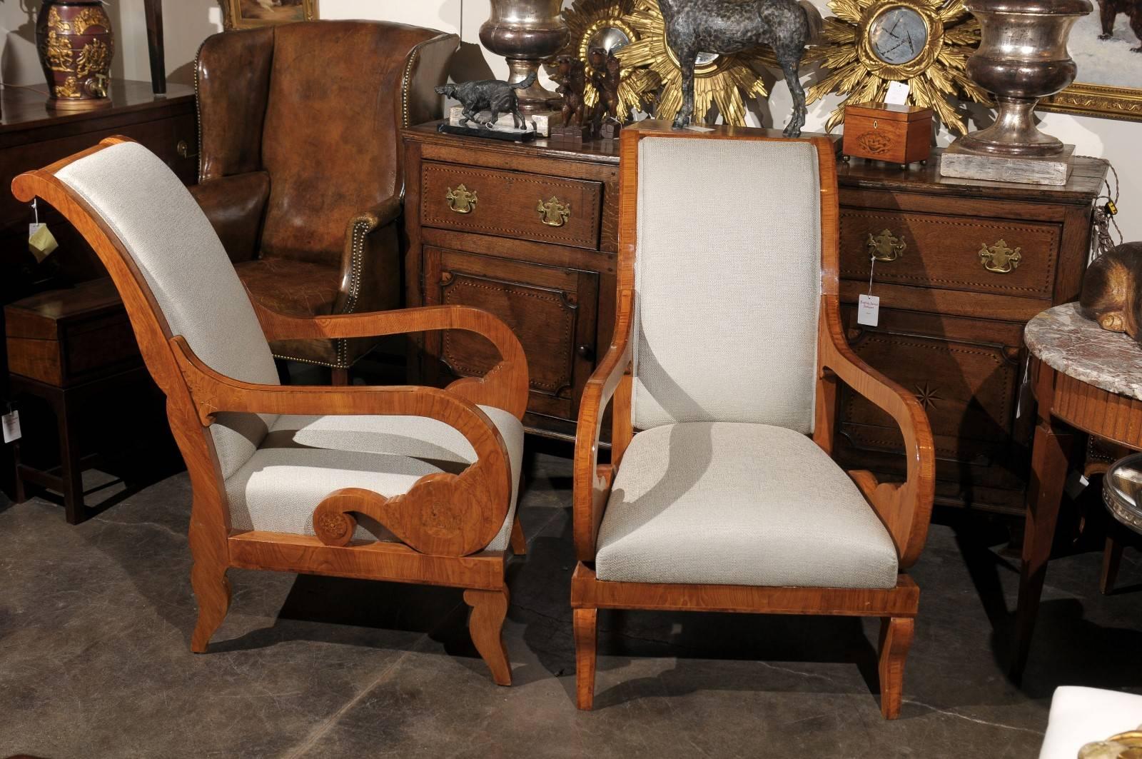 This pair of Austrian upholstered Biedermeier armchairs from the mid 19th century features slanted backs with discreet scrolls in the top rail. The lovely arms are the definite focal point of the ensemble, with their exquisite s-scroll supports and