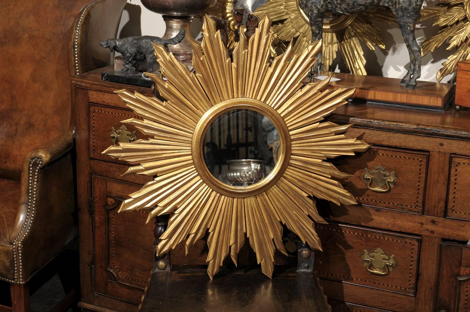 A French vintage round giltwood sunburst mirror. This French mirror from circa 1950 features an exquisite array of sun rays of varying sizes spread out around a central circular mirror. The sun rays are in great condition with a very nice gilding