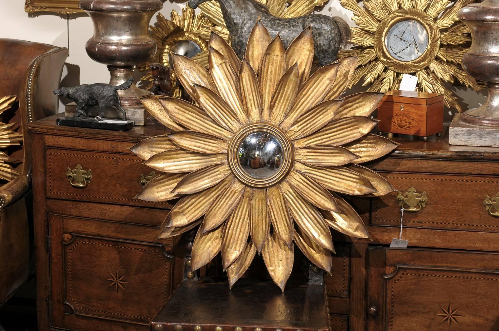 This Spanish sunburst mirror features a circular gilt metal frame with three layers of pointed ribbed petals around a three-banded inner molding enclosing a convex round mirror plate. The figured radiating rays of sunshine can either evoke religious