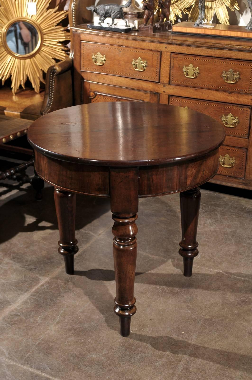An English mid 19th century mahogany center table with a round planked top raised on three elegant baluster-turned legs ending in toupie feet. The plain round apron is only interrupted by the upper cubic parts of the three legs. The beautiful dark