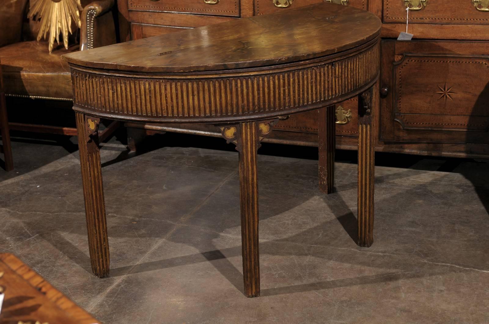 A pair of English Neoclassical style painted wood demi-lune consoles tables with marbleized lift tops, fluted aprons, and straight bracketed legs from the late 19th century. Each of this pair of English demilunes features a semi-circular top with