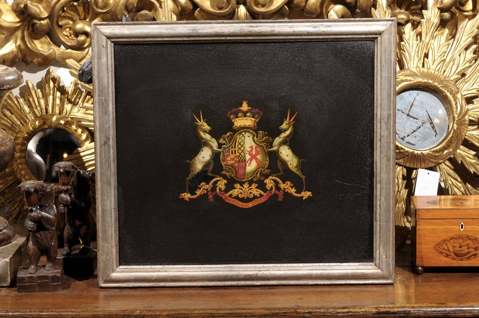 A turn of the century (19th to 20th) English coat of arms painting with silver leaf frame. This English painting from circa 1900 features two antelopes with white coat and red spots flanking a central shield with heraldic decor, topped with a crown.