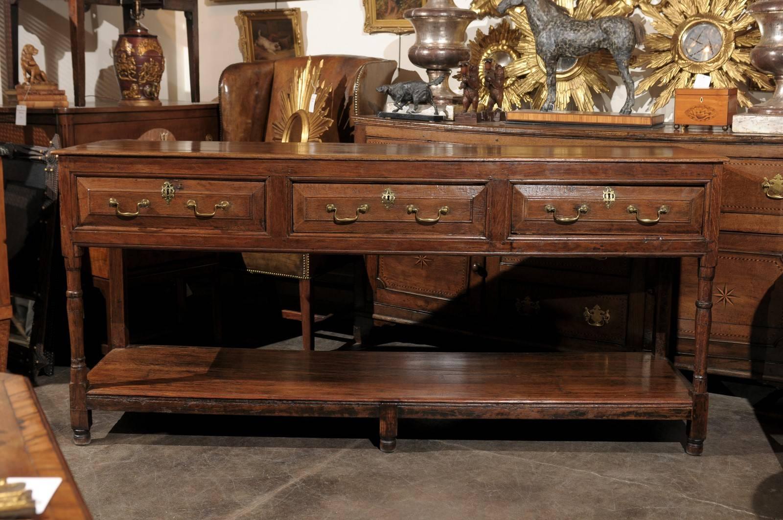 An English Georgian Oak Dresser Base from the early 1800s.  This 19th English Georgian oak dresser base features a rectangular top over three field paneled front drawers, each with two elegant brass swan neck handles flanking a nicely-shaped