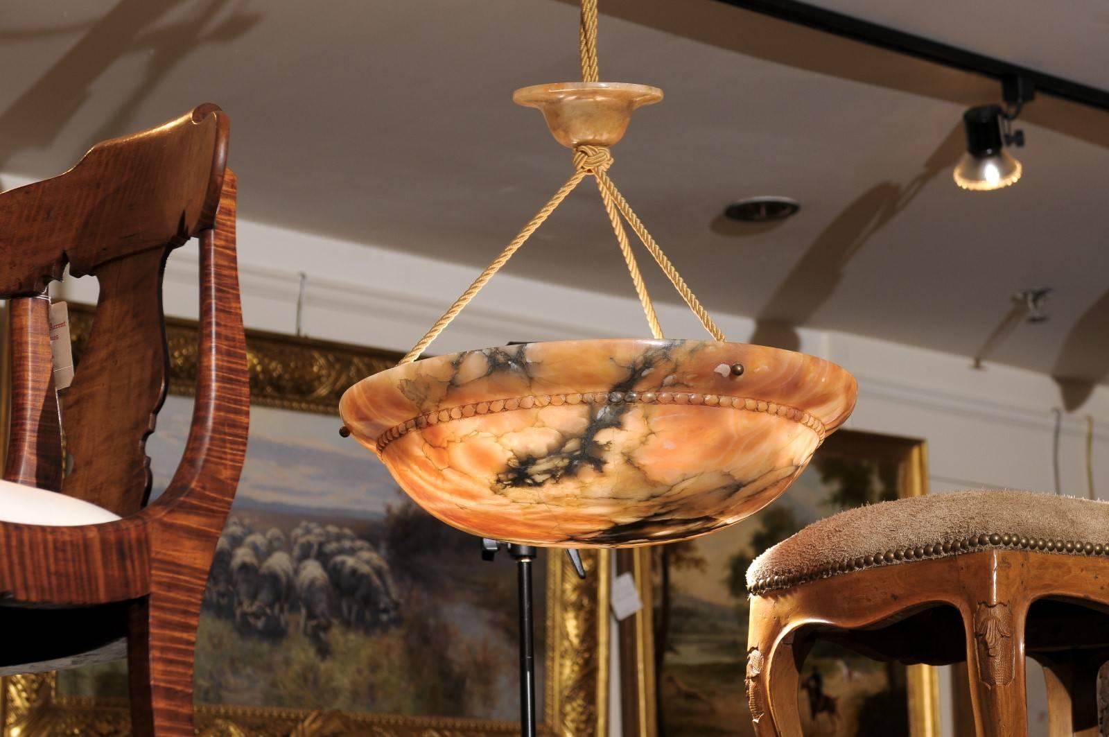 A French Art Deco alabaster light fixture from the 1930s comprising a veined alabaster campaniform bowl carved with a beaded molding, suspended by braided electrified silk cords and a matching alabaster canopy. The highly-figured alabaster polished