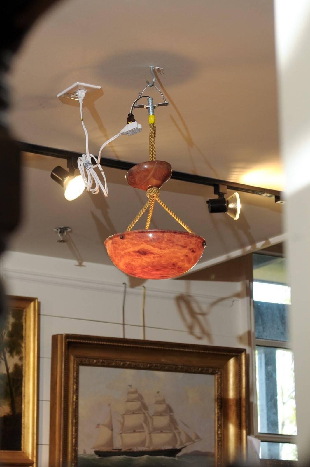 An Art Deco alabaster Swedish light fixture. This orange alabaster small size ceiling hanging light fixture features a curved central bowl suspended to the canopy on cords. The canopy height is adjustable. This warm colored Swedish alabaster pendant