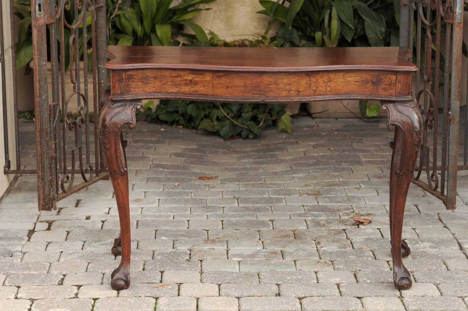 An Italian Rococo walnut console table with serpentine front from the late 18th century. This stylish Italian console circa 1790 features a serpentine front resting on four cabriole legs with delicately carved volutes on the knees and ball-and-claw