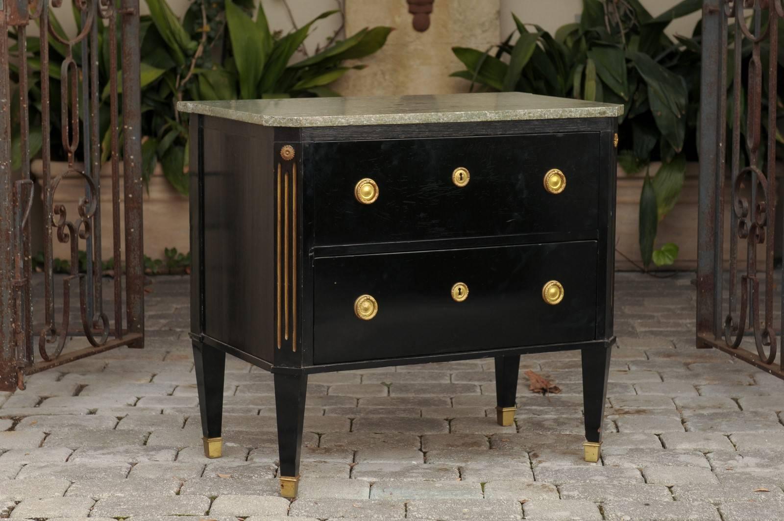 An elegant 19th century Austrian Biedermeier parcel-gilt and ebonized petite chest of drawers presenting a rectangular grey marble top with slanted corners above two drawers resting on tapered legs and brass feet. This chest features canted corners