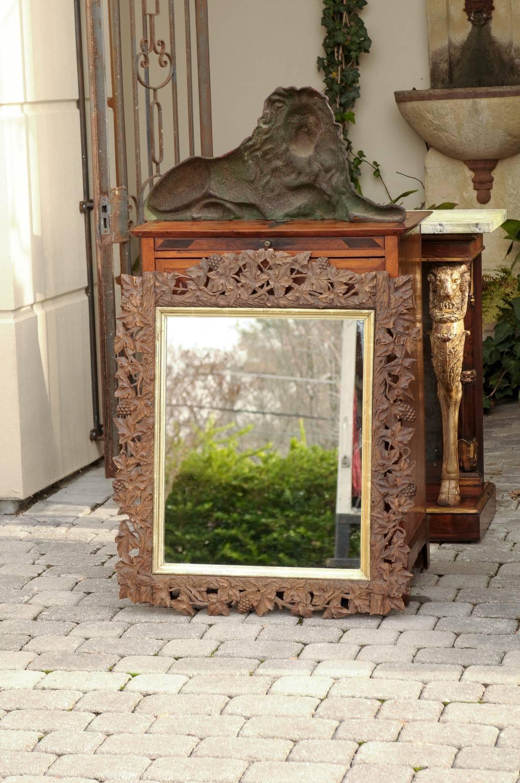 This late 19th century French mirror is set within a thin gilt molded frame enclosed in a rectangular Black Forest style carved crested wooden frame. The intricate decor is composed of beautifully detailed openwork intertwined vines with leaves and