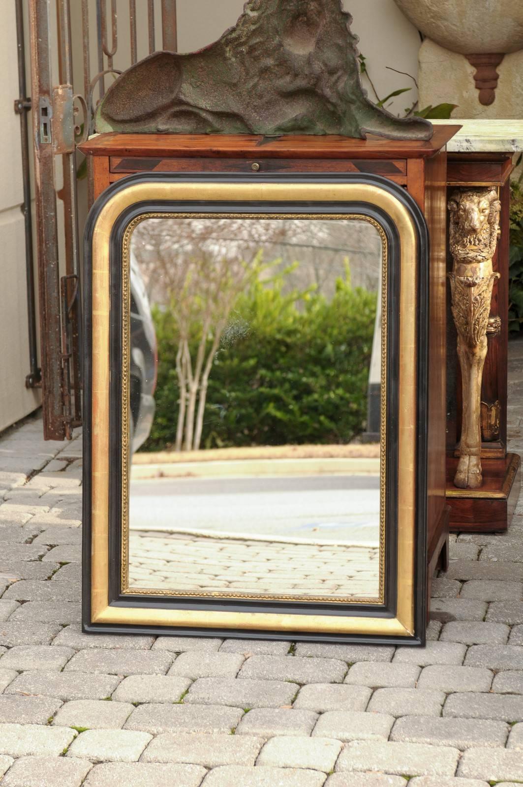 A French wooden black and gold Louis-Philippe style mirror from the beginning of the 20th century set within a rectangular frame with characteristic rounded top corners and square base. Two ebonized moldings intersperse with a gilt middle one, with