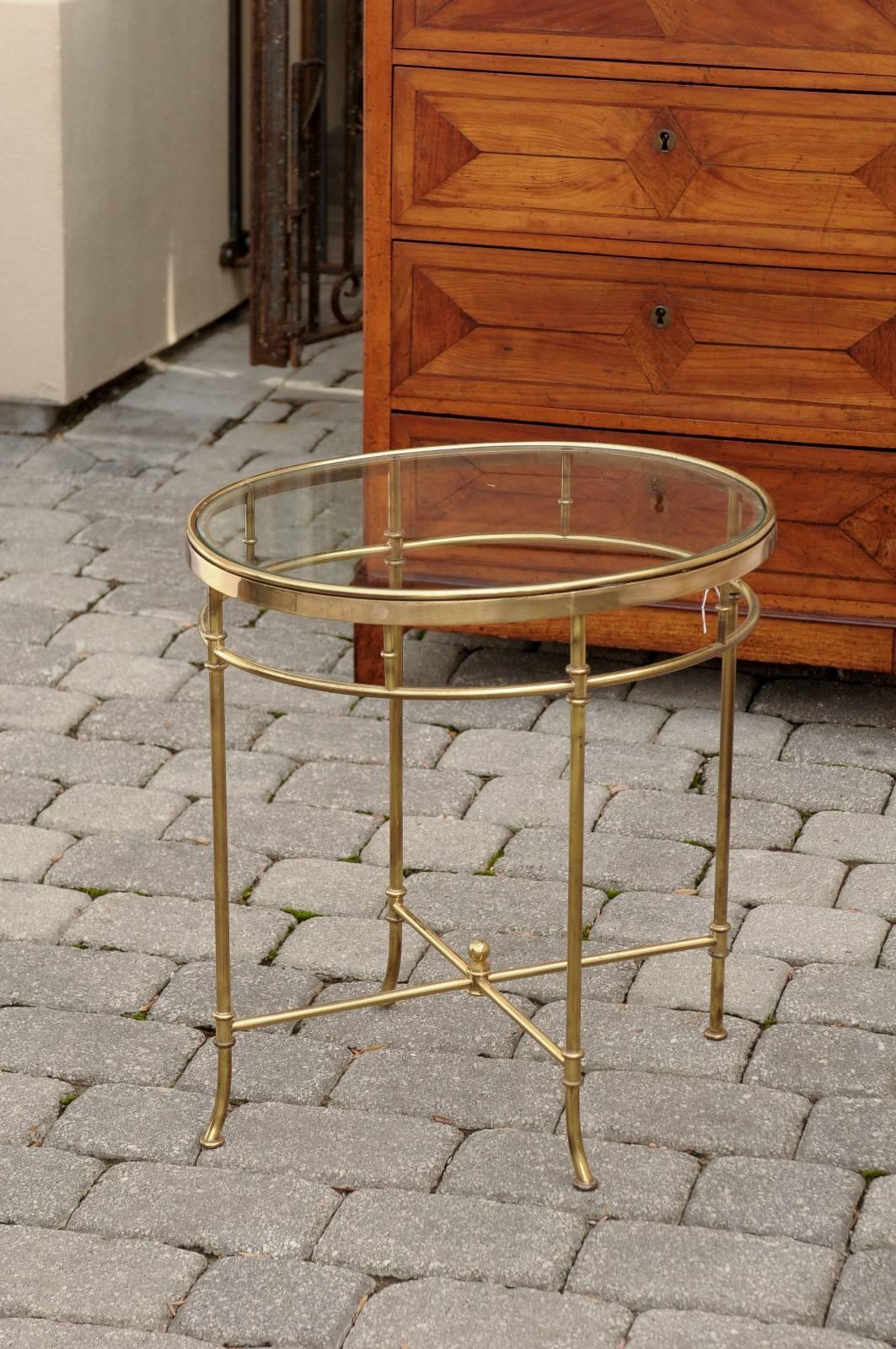 An Italian mid century brass and glass top oval side table. This Italian vintage side table features an oval glass top set into a brass frame. Four thin legs support the structure. They are connected at the top with a thin brass ring and at the