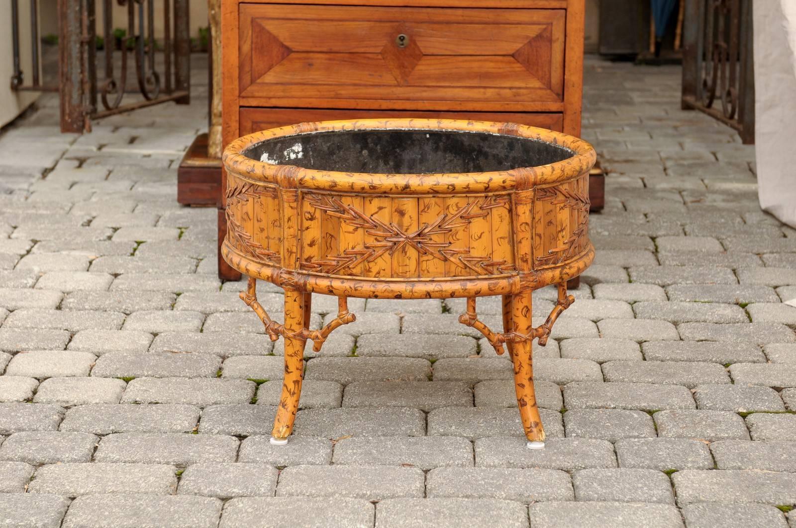 This French jardinière features a circular shaped made of faux-bamboo and is lined with metal on the inside. The planter is adorned on its surround with a wonderful faux-bamboo motif that includes wood, knots and stitches and is raised on four short