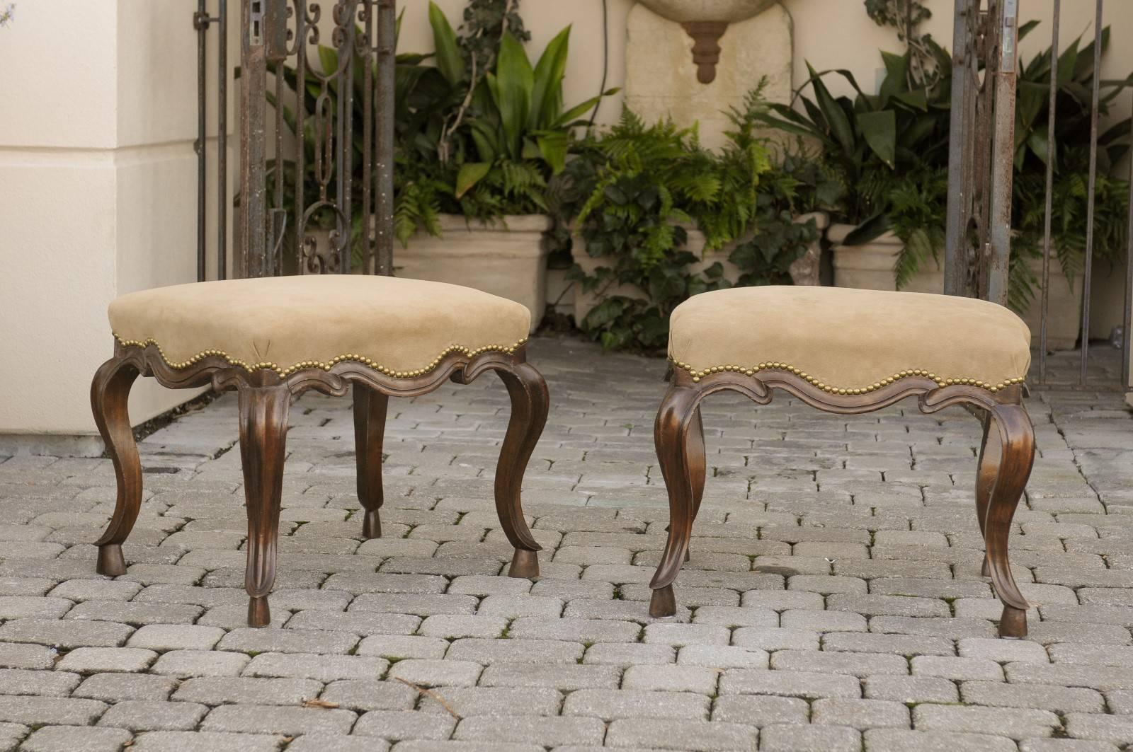 An exquisite pair of 19th century Italian walnut stools. This pair of Italian stools features four dark wood cabriole legs delicately profiled and raised on hoofed feet. The upholstery used is a light brown Suede with nailhead surround. With its