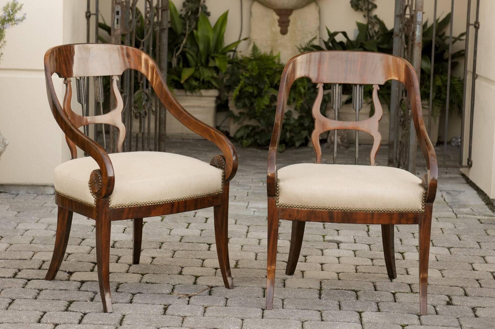 A pair of Austrian Biedermeier armchairs from the mid 19th century with arrow motifs, scrolled arms and upholstered seats. Each of this pair of Biedermeier armchairs features an exquisite curved back adorned with two dark colored arrows pointing