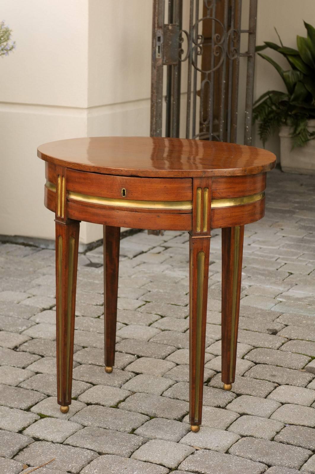 19th century Russian mahogany oval side table with vertical and horizontal brass inlaid elements.  This mahogany side table features an oval top over a frieze drawer resting on four tapered fluted legs with brass inlays and brass ball feet. A thick