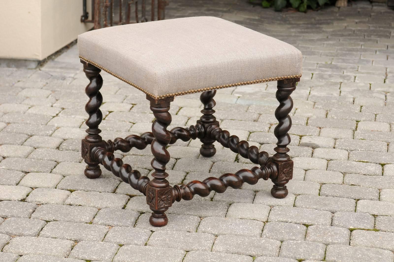 An English barley twist stool from the late 19th century. This elegant English upholstered ottoman stands on four barley twist legs with four barley twist side stretchers. Each leg is decorated with elegant rosettes where the stretchers come