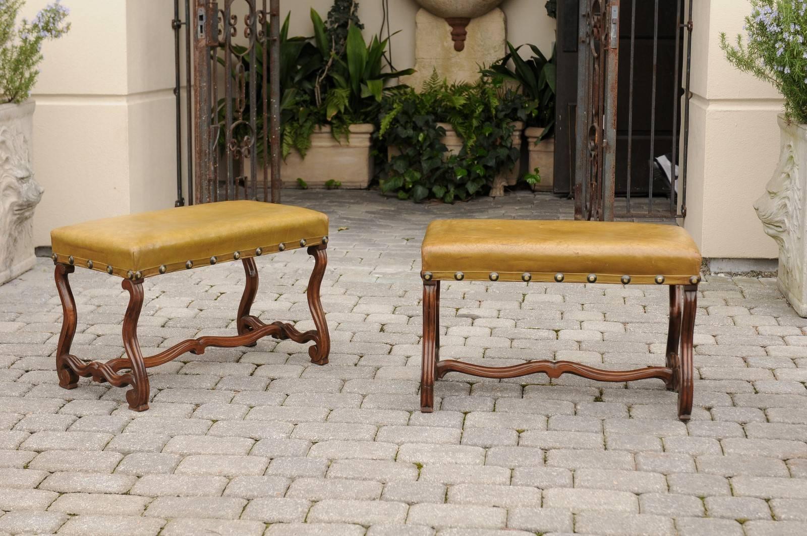This stylish pair of French 19th century walnut stools or benches features rectangular leather upholstered seats with nailhead surround, over an os de mouton frame: the Louis XIII style body is indeed made of four mutton legs with sinuous cross and