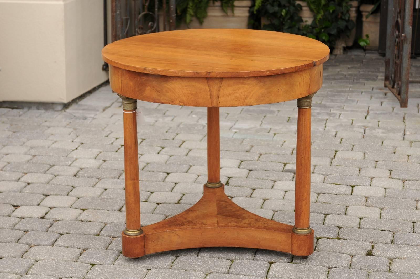 An Austrian Biedermeier center table from the mid-19th century. This Biedermeier center table from circa 1840 features a round top over a simple recessed apron, supported by a tripod base. The three legged base is made of elegant bronze-mounted