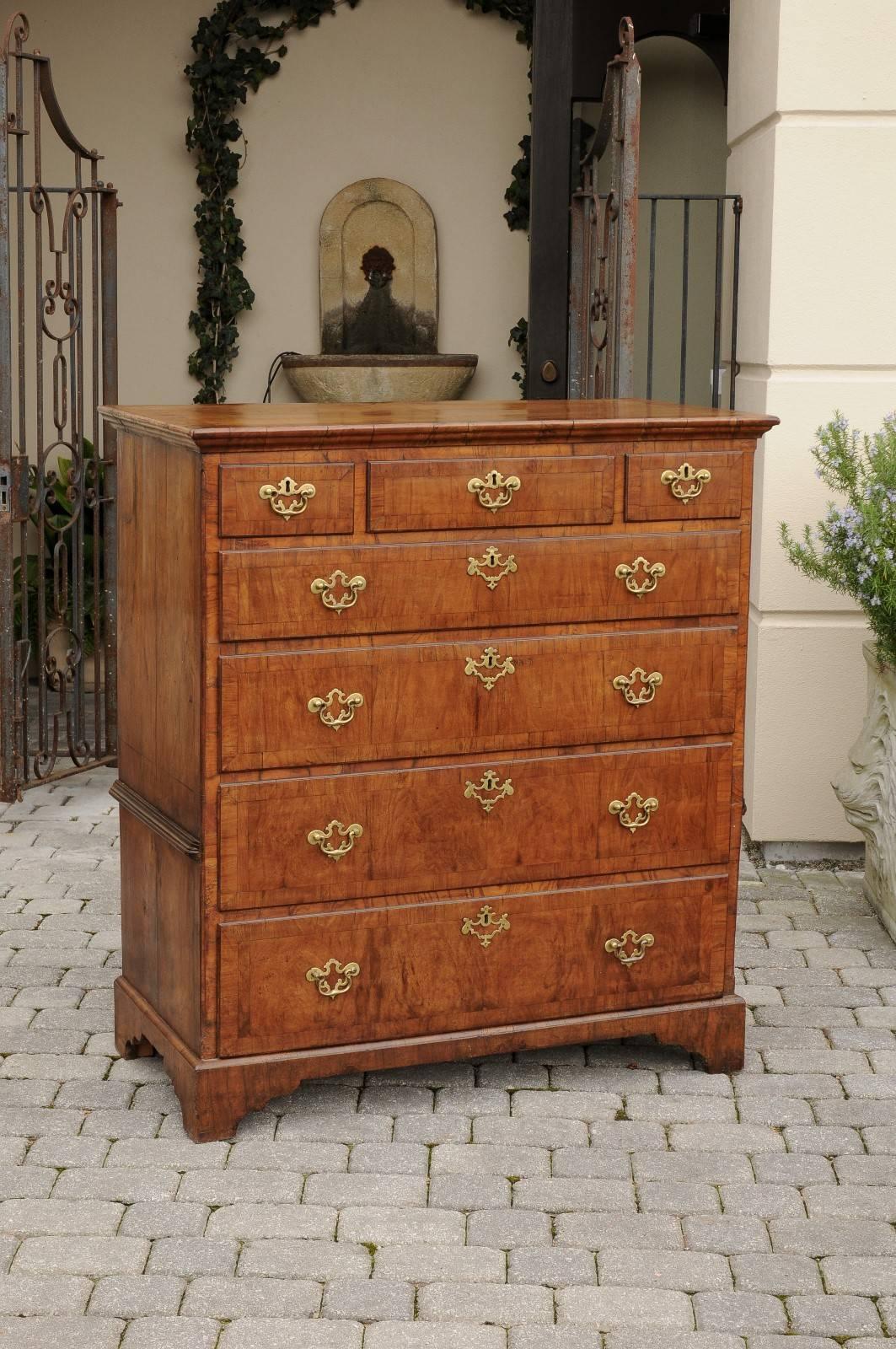 An English walnut seven-drawer chest from the early 19th century. This English chest of drawers features an exquisite two-toned rectangular butterfly veneered top over seven graduated drawers. Four full width drawers sit below three smaller drawers