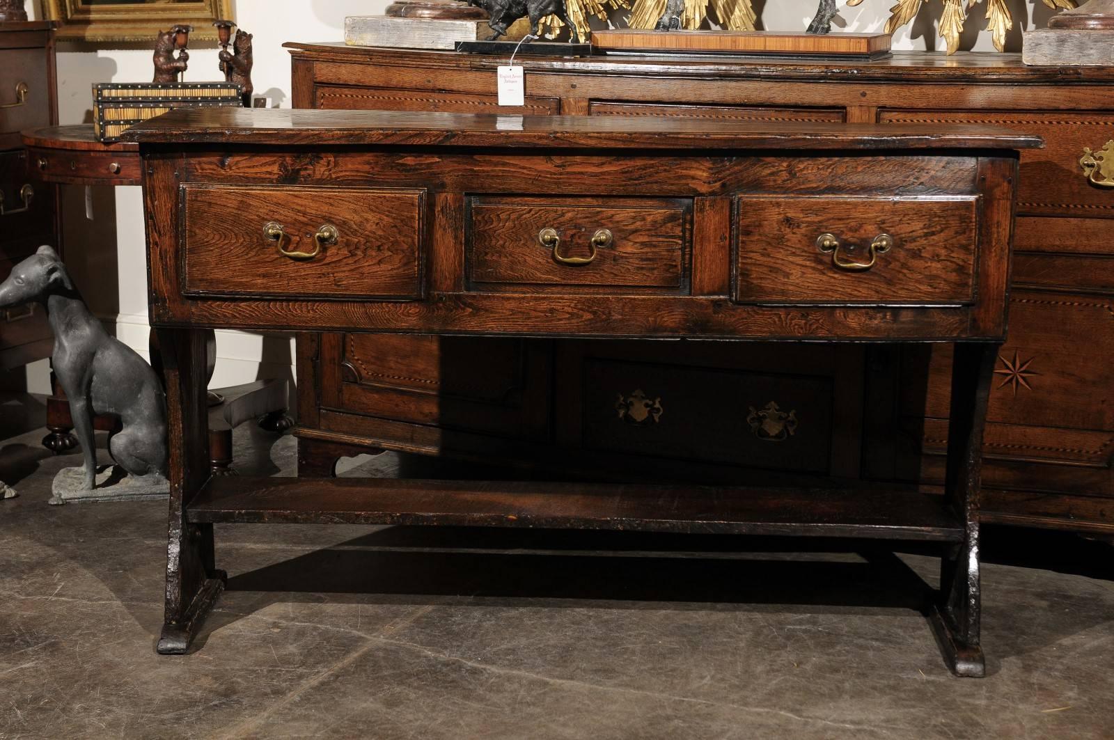 This exquisite small size English server or dresser base from the 18th century features a rectangular top over three drawers opening with brass bail handles. The server is raised on a trestle base with lower shelf, ready to showcase any beautiful