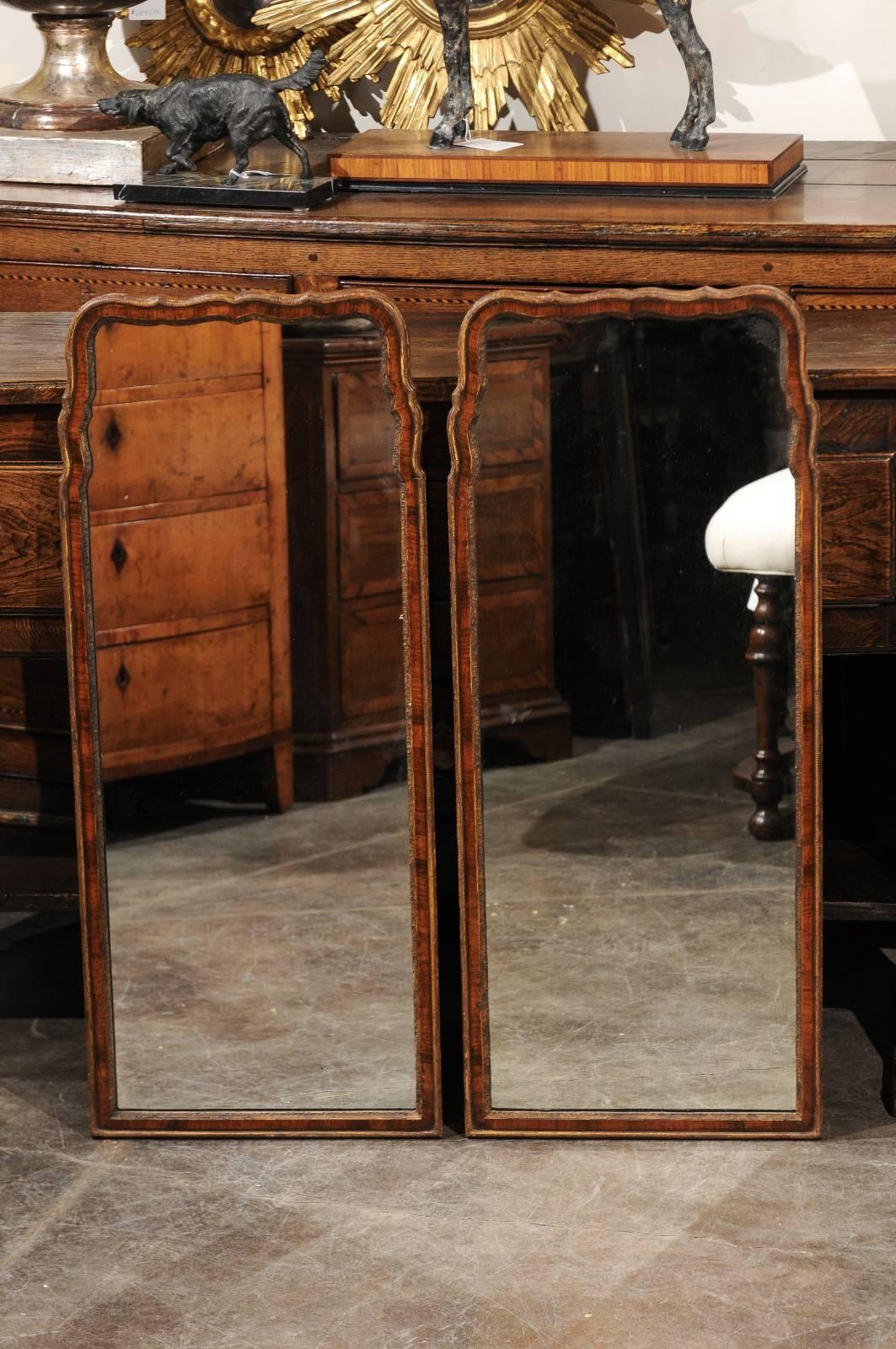 A pair of late 19th century English Queen Anne style narrow mirrors. This pair of English walnut mirrors from circa 1880 features a nice vertical, narrow Silhouette. The crest is curved, in typical Queen Anne manner. The frame is made of burled