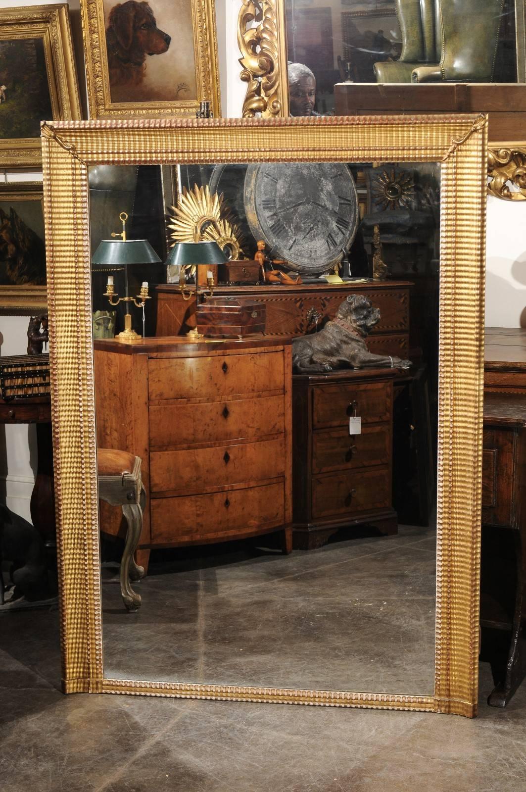 A large French rectangular giltwood mirror from the turn of the century. This French mirror, circa 1900 (or earlier) is made of a gilded rectangular ridged wooden frame, adorned with delicate foliage motifs in the top corners. The central part, made