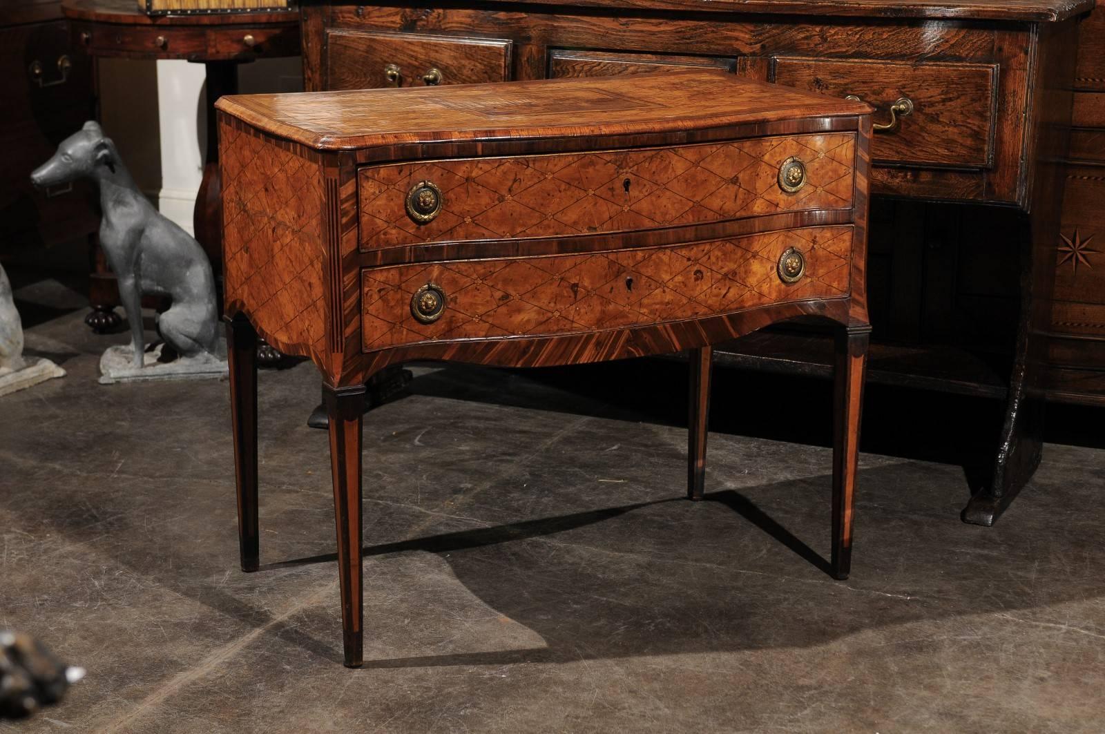 This Italian 18th century chest features an exquisite top adorned with a diamond pattern veneer, around a central landscape scene in marquetry. The horizontal diamond pattern is repeated on both the sides and the front. Two delicate drawers fill the