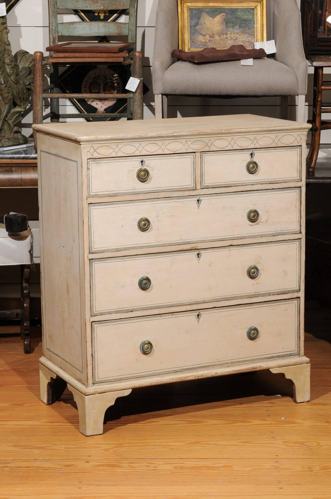 This English painted wood chest of drawers from the 19th century features five graded drawers, with the shallowest at the top, and the deepest at the bottom. This original off-white color English chest shows quite a linear profile with clean