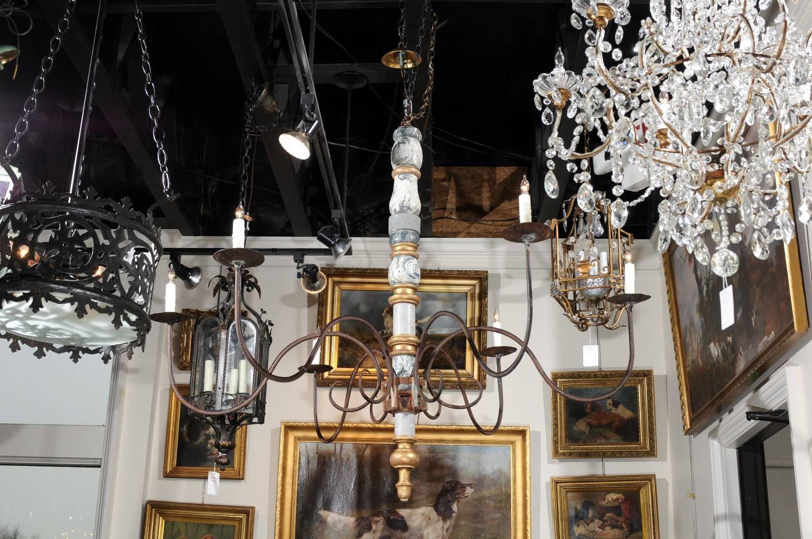 This turn of the century (19th to 20th) Italian candelabra style chandelier features a central painted and gilded wooden column, from which six iron swoop arms radiate. The thin arms support the metal bobèches as well as new authentic wax candle