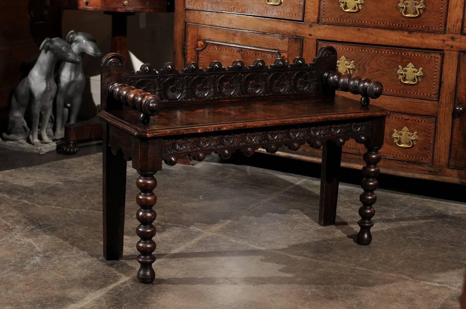 This exquisite English wooden window bench features a low carved back decorated with medallions, a decorative motif that is echoed in the front skirt. The single plank wooden seat is chamfered on the sides. The spool arms and bobbin front legs