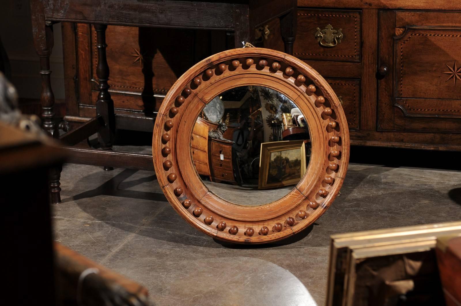 This English girandole convex mirror is made of a round pine frame, decorated with a ring of small decorative balls on the surround. This early 19th century mirror features a particularly trendy convex mirror, slightly distorting the reflection of