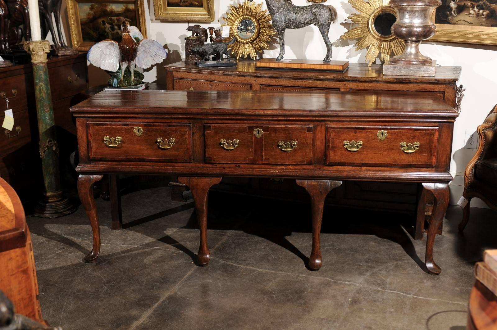 This English Georgian oak server / dresser base from the early 19th century features a rectangular top with banding over three drawers with brass bail handles and solid backplate. The drawers are also adorned with a thin banded veneer in the