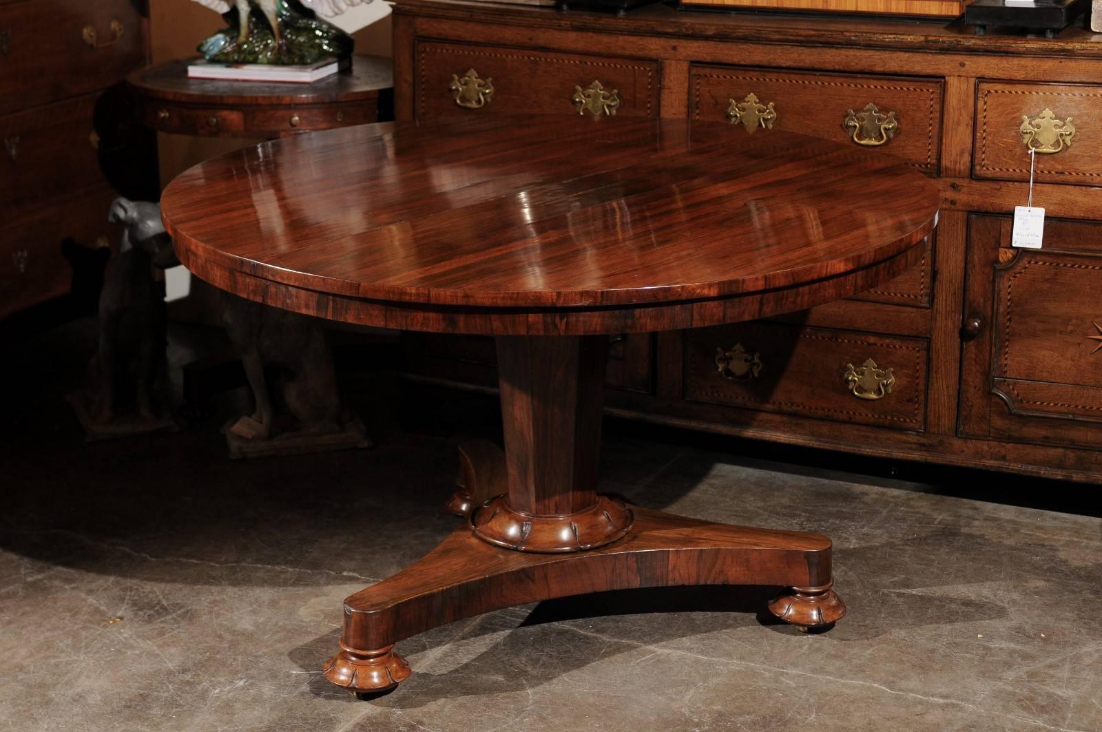 This English rosewood pedestal centre table from the mid-19th century features a stunning circular top, which tilts, over an elegant central tapered pedestal. The junction between the pedestal and the tripod base is decorated with a carved