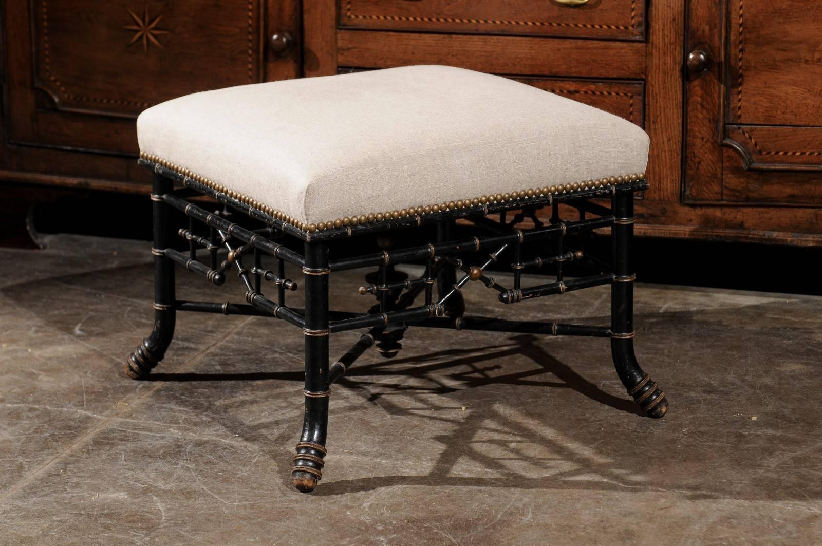 This English Chinese Chippendale style late 19th century upholstered stool is made of an ebonized faux-bamboo frame supporting a square shaped seat. The muslin upholstery is secured on the surround by a trim of nail heads. The exquisite base