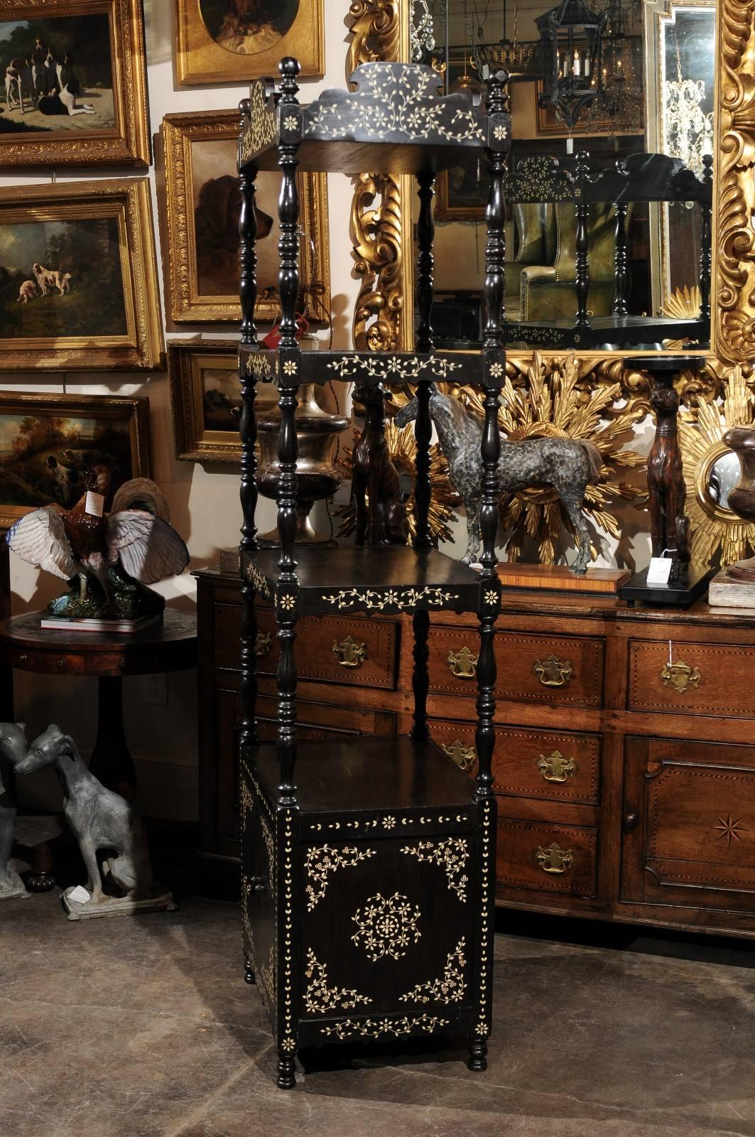 This delicate ebonized wood etagère / trolley from the early 19th century features a carved top over three open shelves. The fully enclosed lower section is accessed by two doors that open to reveal a nice storage compartment. The top and shelves
