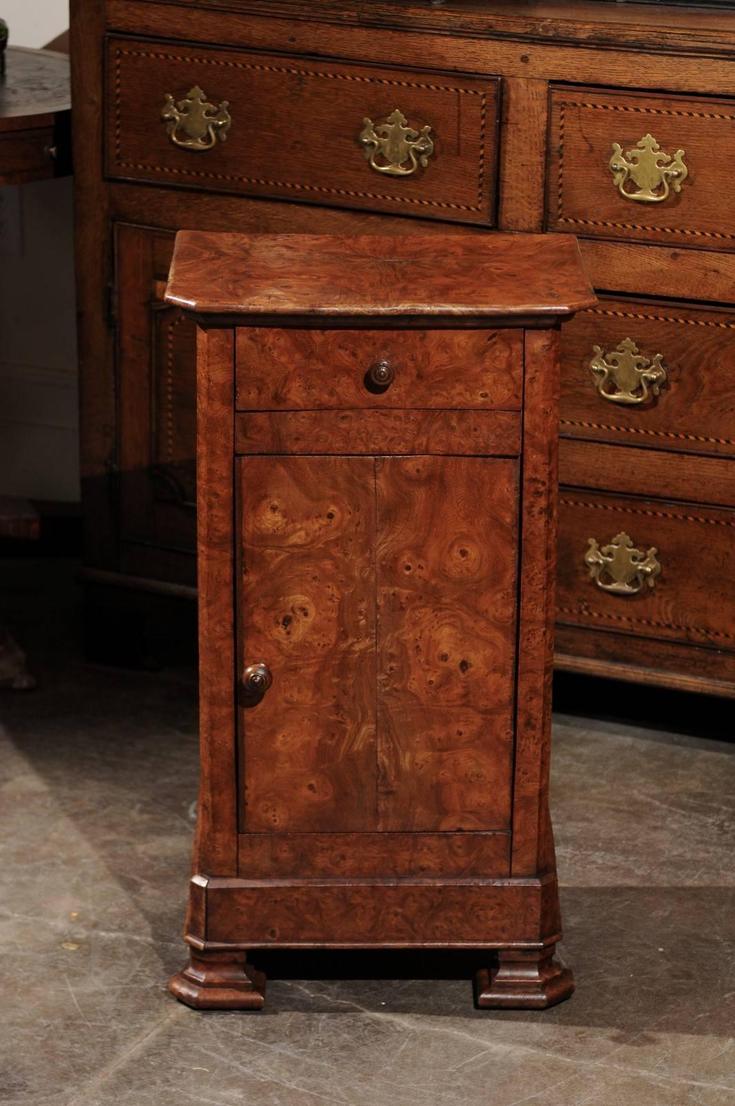 This English burl wood pot cupboard from the late 19th century features a rectangular top with chamfered front corners over a single drawer above a cabinet door, both adorned with a single wooden pull. Raised on two nicely carved front feet and