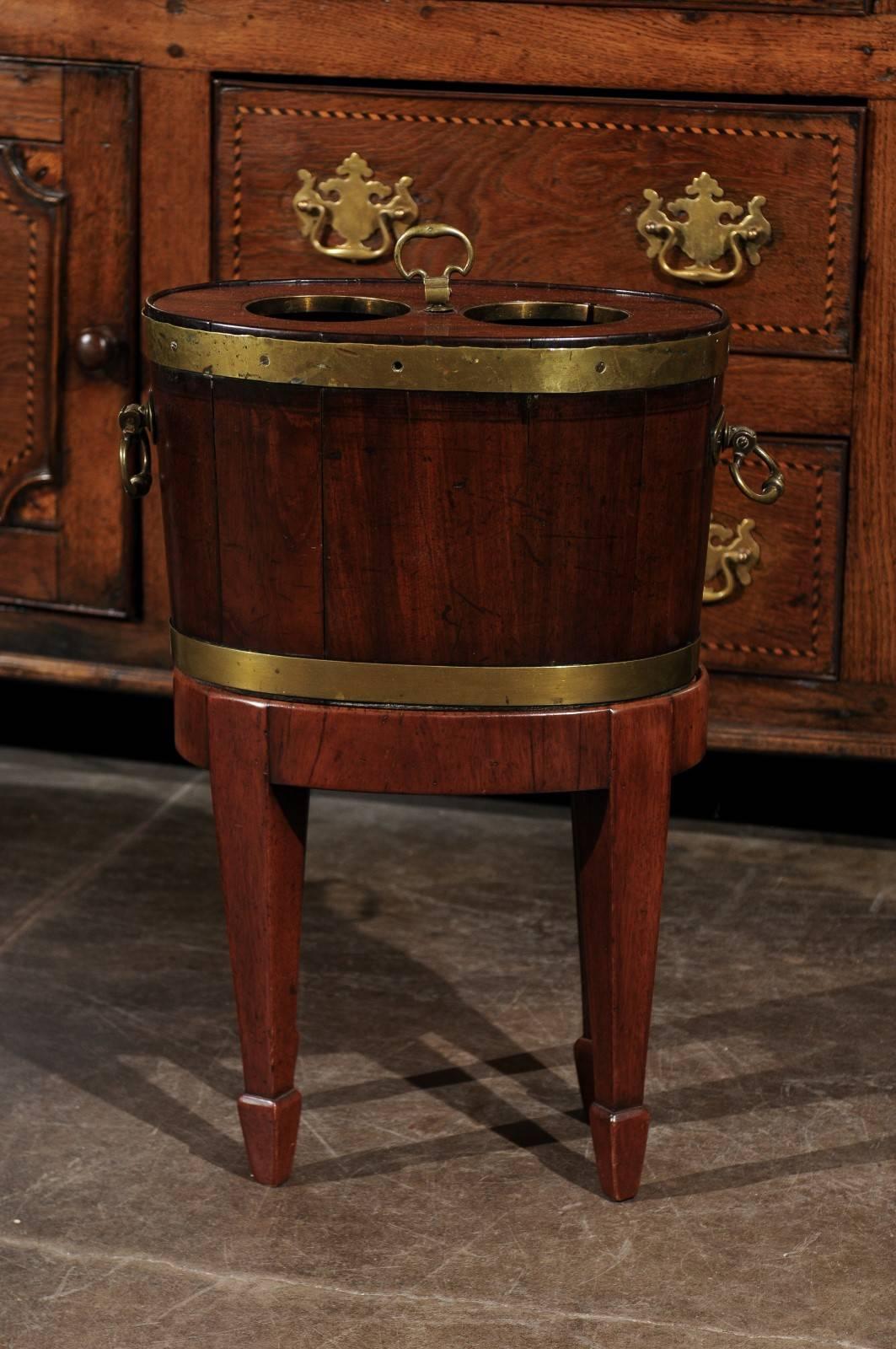 An English mahogany and brass wine cooler from the mid-19th century. This wood and brass wine cooler features a lead lining that would have kept wine or champagne cool. The top is made of a removable wooden cover with two circular holes cut-out from