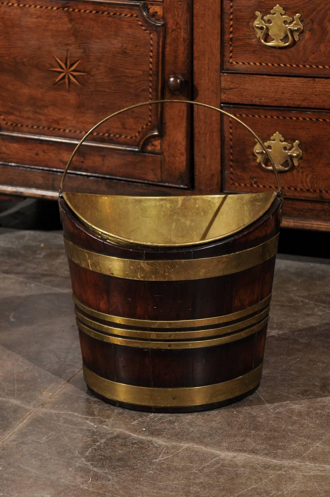 A 19th century English wooden peat bucket with brass lining. This mahogany peat bucket is secured by five brass bands, two wider ones at the top and the bottom and three narrow ones in the center. Peat buckets were common in England and Ireland