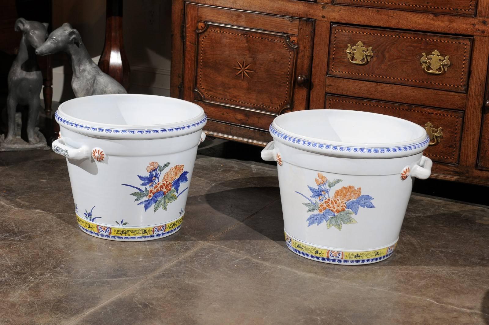 This pair of French faience cache pots or jardinières from the mid-20th century feature round and white bodies, adorned with blue lining decor on the lips as well as exquisite hand-painted bouquets of flowers in the center with blue, green and